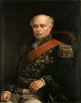 Paez is depicted sitting on a dark chair in a dark space, wearing black, red, and gold military dress.